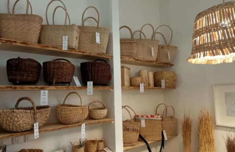 Półki na których prezentują się kosze z różnych materiałów - wiklina, słoma, torebki z rogożyny