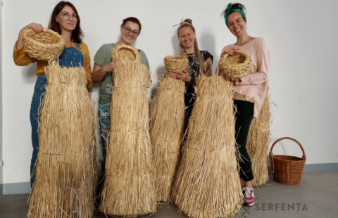 Warsztaty wyplatania ze słomy Serfenta, uczestniczki prezentują prace, stojąc przy snopkach słomy
